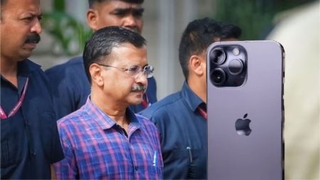 Arvind Kejriwal holding an iPhone with a puzzled expression